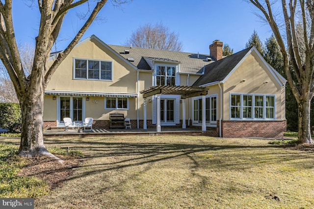 back of property featuring brick siding, stucco siding, a lawn, a patio area, and a pergola