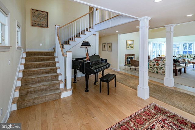 interior space with recessed lighting, stairway, light wood finished floors, a glass covered fireplace, and ornate columns