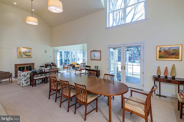 dining room with french doors, a fireplace, light colored carpet, high vaulted ceiling, and baseboards