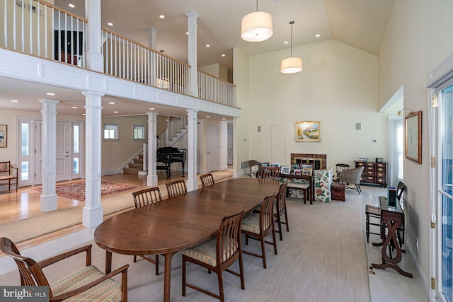 dining space featuring a brick fireplace, decorative columns, stairway, and a towering ceiling