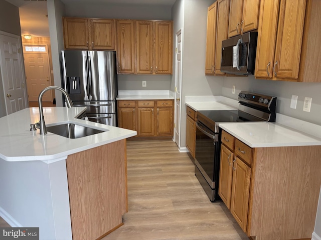 kitchen featuring brown cabinets, a center island with sink, light wood finished floors, appliances with stainless steel finishes, and a sink