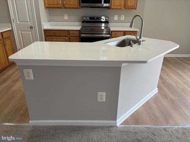 kitchen featuring appliances with stainless steel finishes, a kitchen island with sink, brown cabinetry, and a sink