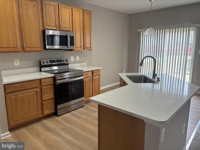 kitchen with light wood-type flooring, appliances with stainless steel finishes, brown cabinets, and a sink