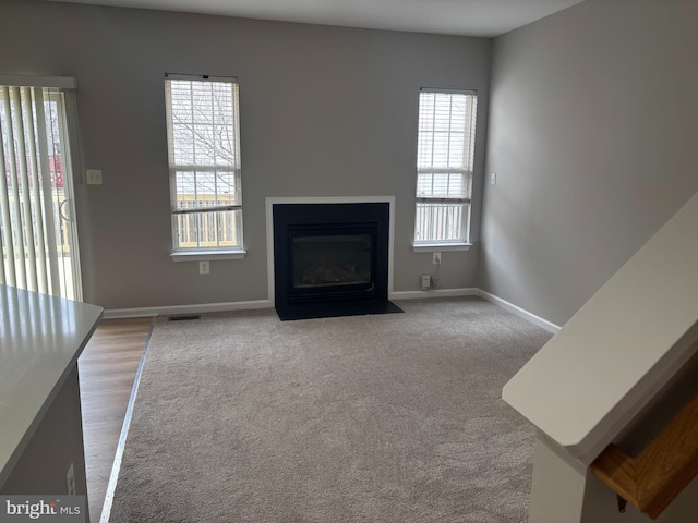 unfurnished living room with carpet floors, a fireplace with flush hearth, and baseboards