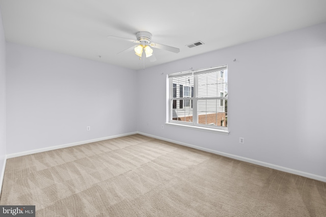 carpeted empty room with baseboards, a ceiling fan, and visible vents