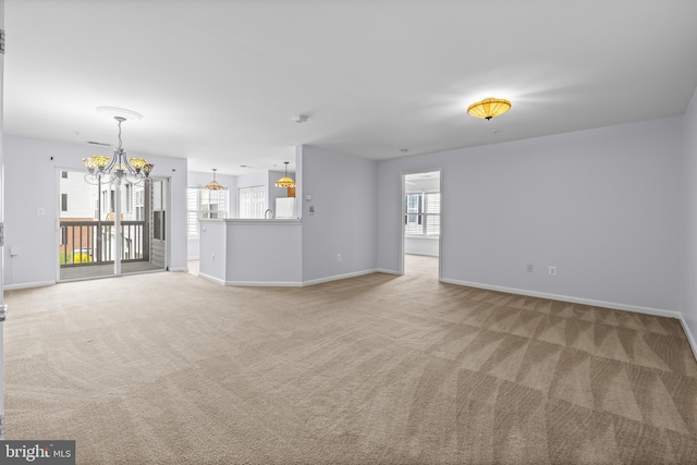 unfurnished living room featuring baseboards, an inviting chandelier, light colored carpet, and a healthy amount of sunlight