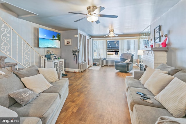 living room with ceiling fan, radiator heating unit, a brick fireplace, and wood-type flooring