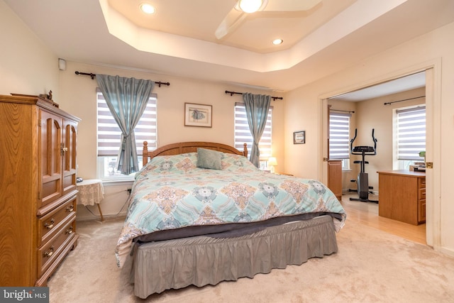 bedroom with multiple windows, a tray ceiling, and light carpet