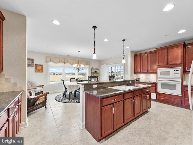 kitchen with white appliances, a wealth of natural light, hanging light fixtures, and dark stone countertops