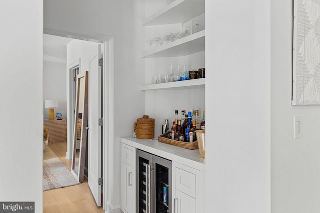 bar with wine cooler, light wood-style flooring, and a bar