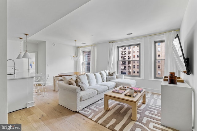 living area with visible vents, plenty of natural light, light wood-style flooring, and baseboards