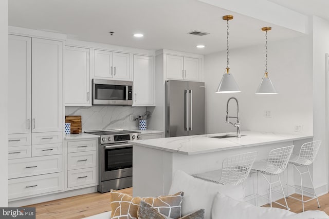 kitchen featuring light stone counters, stainless steel appliances, hanging light fixtures, white cabinets, and a kitchen breakfast bar