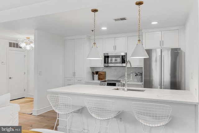 kitchen with light stone countertops, white cabinetry, appliances with stainless steel finishes, and pendant lighting