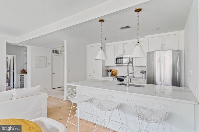 kitchen featuring visible vents, white cabinets, stainless steel appliances, pendant lighting, and a sink