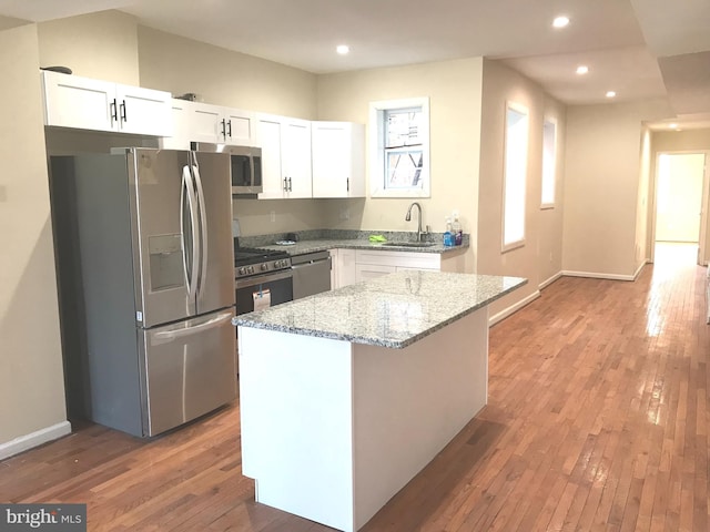 kitchen with a kitchen island, appliances with stainless steel finishes, white cabinets, light stone countertops, and light hardwood / wood-style flooring