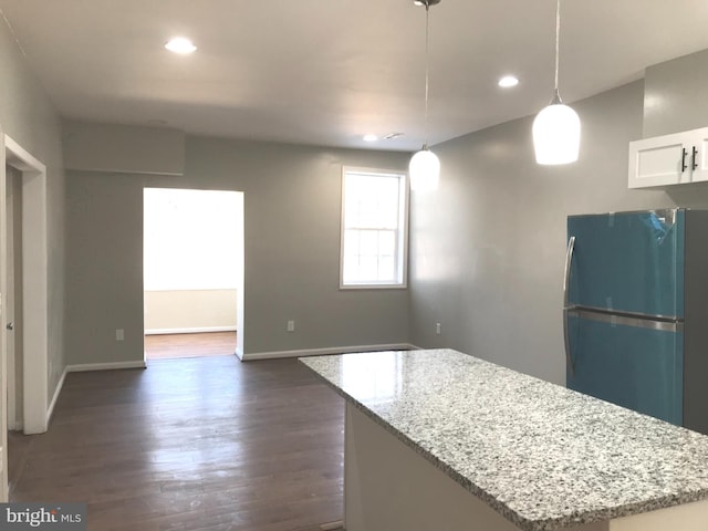 kitchen featuring white cabinetry, hanging light fixtures, black refrigerator, a center island, and light stone counters