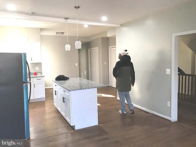 kitchen with stainless steel fridge, white cabinetry, hanging light fixtures, a center island, and light stone counters