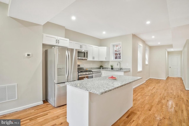 kitchen with light stone counters, stainless steel appliances, a center island, and white cabinets