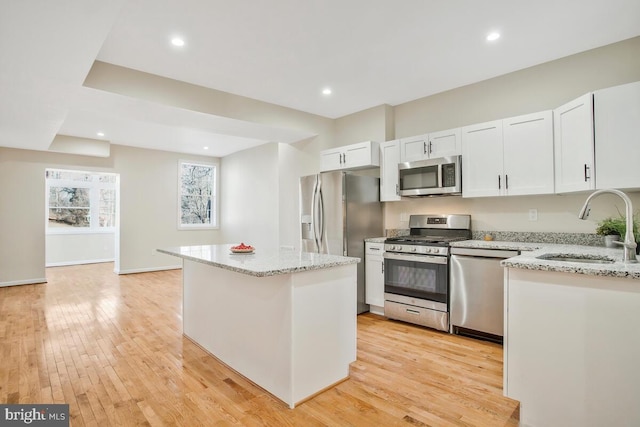 kitchen featuring sink, appliances with stainless steel finishes, white cabinetry, light stone counters, and a kitchen island