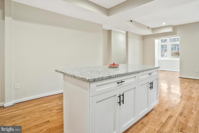 kitchen with white cabinetry, a center island, light hardwood / wood-style floors, a tray ceiling, and light stone countertops