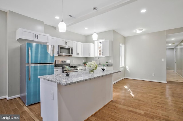 kitchen with pendant lighting, white cabinetry, light stone counters, stainless steel appliances, and light hardwood / wood-style flooring