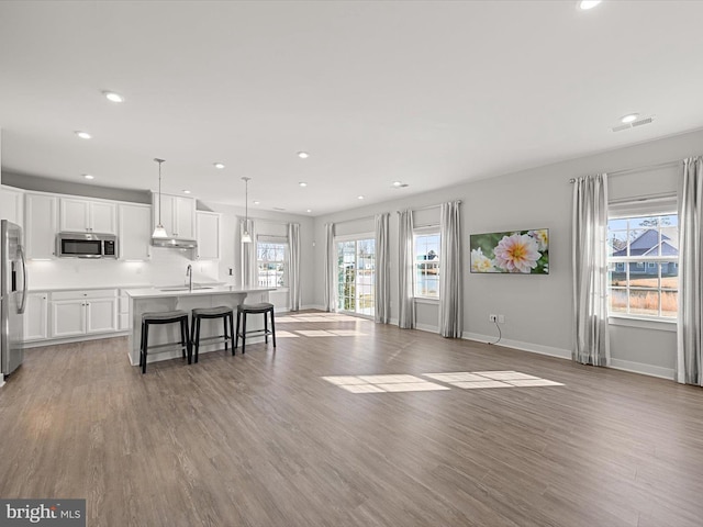 kitchen featuring white cabinetry, a breakfast bar area, hanging light fixtures, a kitchen island with sink, and stainless steel appliances