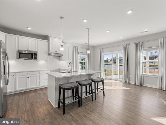 kitchen featuring pendant lighting, sink, white cabinetry, stainless steel appliances, and a center island with sink