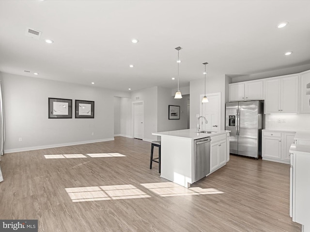 kitchen with sink, a kitchen island with sink, stainless steel appliances, white cabinets, and decorative light fixtures