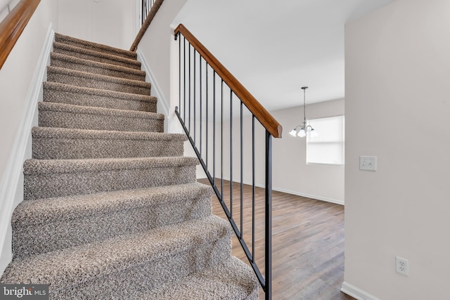 stairway featuring an inviting chandelier and wood-type flooring