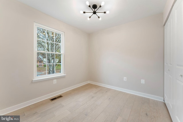 empty room featuring a notable chandelier and light hardwood / wood-style flooring