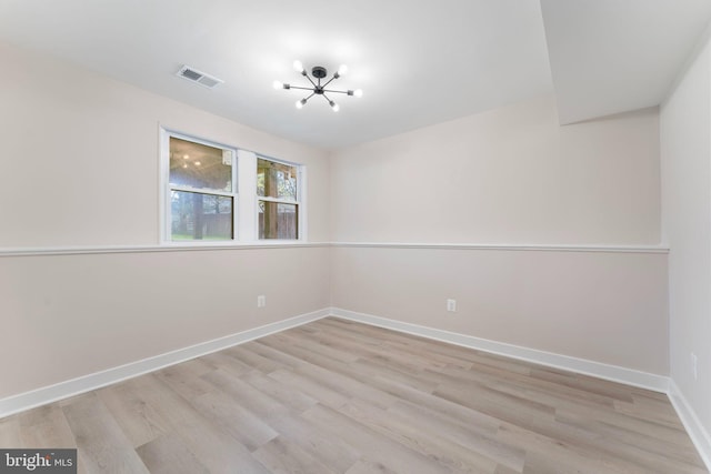 spare room with an inviting chandelier and light wood-type flooring