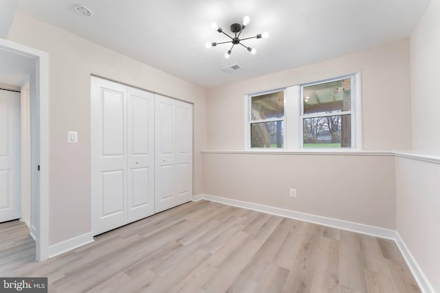 unfurnished bedroom featuring a closet, a chandelier, and light wood-type flooring