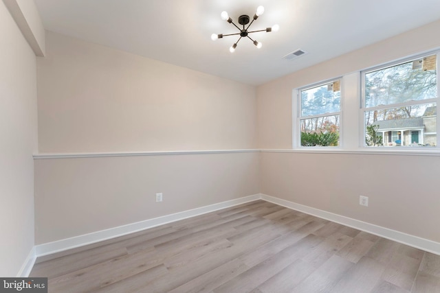 empty room with an inviting chandelier and light hardwood / wood-style flooring