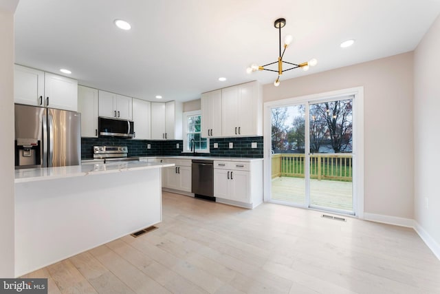 kitchen with decorative light fixtures, white cabinets, decorative backsplash, stainless steel appliances, and light wood-type flooring