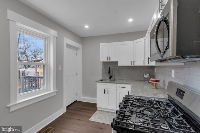 kitchen featuring appliances with stainless steel finishes, dark hardwood / wood-style floors, sink, white cabinets, and light stone countertops