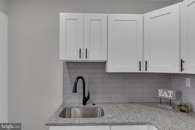 details with white cabinetry, tasteful backsplash, sink, and light stone counters