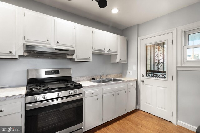 kitchen with stainless steel gas stove, light countertops, a sink, and under cabinet range hood