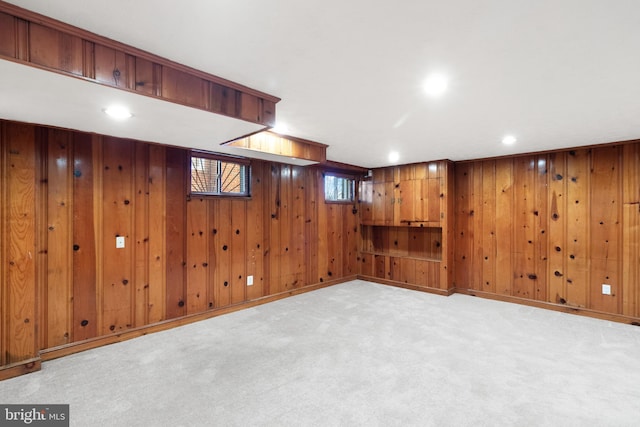 below grade area with baseboards, wooden walls, recessed lighting, and light colored carpet