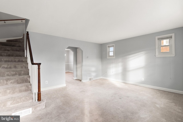 unfurnished living room with arched walkways, visible vents, carpet flooring, baseboards, and stairs