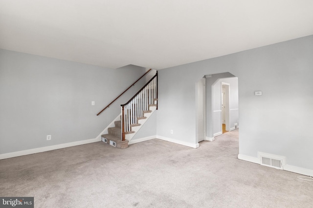 interior space with light colored carpet, arched walkways, visible vents, and stairs