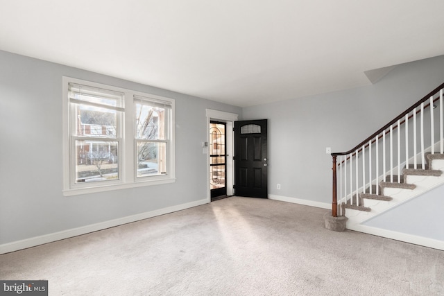 carpeted foyer featuring stairway and baseboards