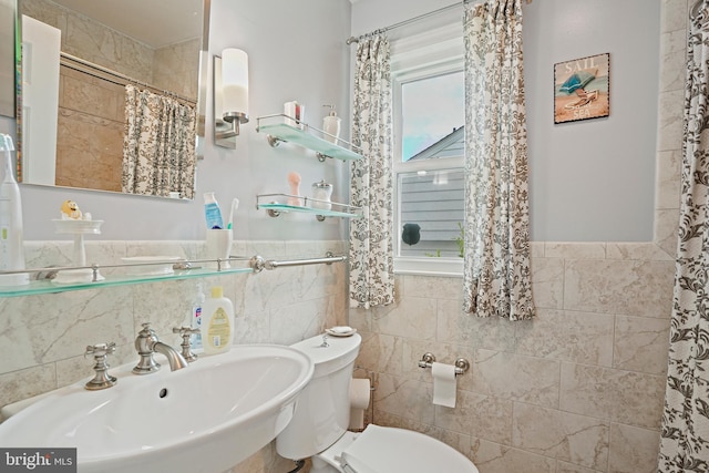 bathroom with walk in shower, toilet, sink, and tile walls