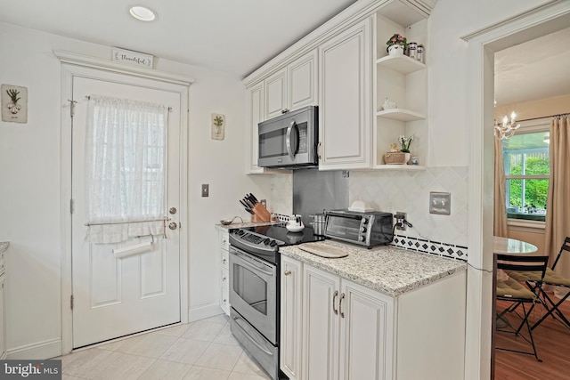 kitchen with white cabinetry, light stone counters, a chandelier, appliances with stainless steel finishes, and decorative backsplash