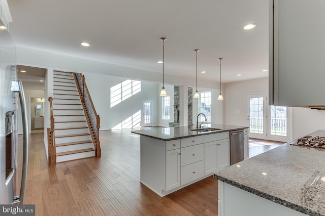 kitchen with dishwasher, pendant lighting, dark stone counters, a kitchen island with sink, and white cabinets