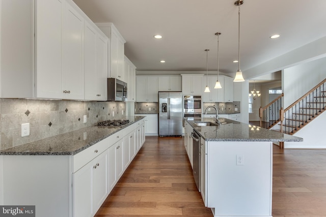 kitchen featuring sink, decorative light fixtures, appliances with stainless steel finishes, an island with sink, and white cabinets