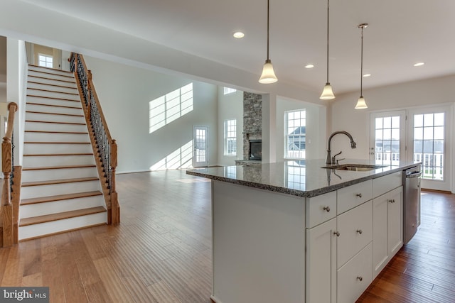 kitchen with sink, hanging light fixtures, an island with sink, white cabinets, and dark stone counters