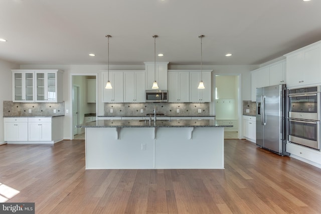 kitchen featuring white cabinetry, appliances with stainless steel finishes, dark stone countertops, and a kitchen breakfast bar