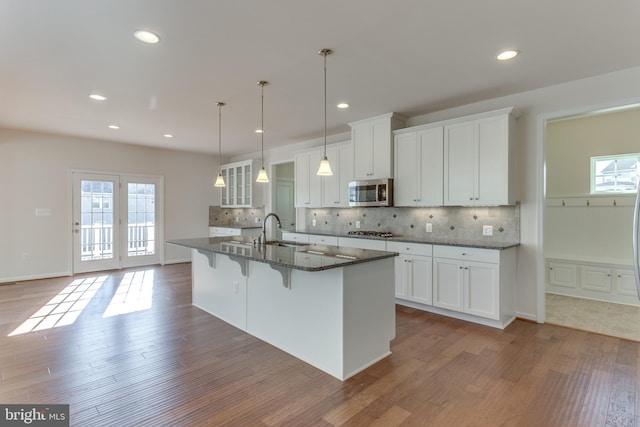 kitchen with sink, appliances with stainless steel finishes, dark stone countertops, white cabinetry, and an island with sink