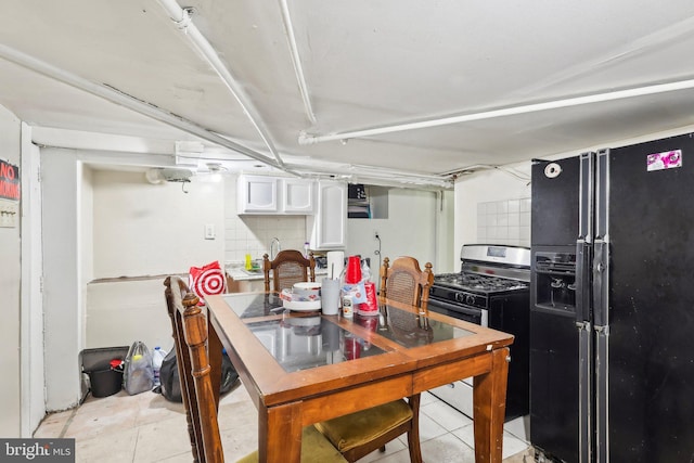 kitchen featuring stainless steel range with gas stovetop, white cabinets, decorative backsplash, light tile patterned flooring, and black fridge