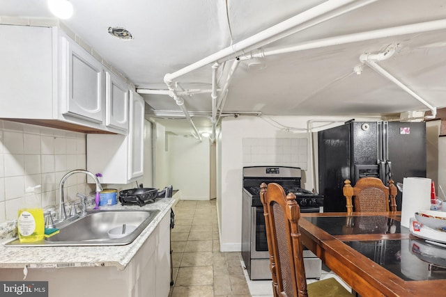 kitchen featuring white cabinetry, backsplash, stainless steel range with gas cooktop, sink, and black fridge